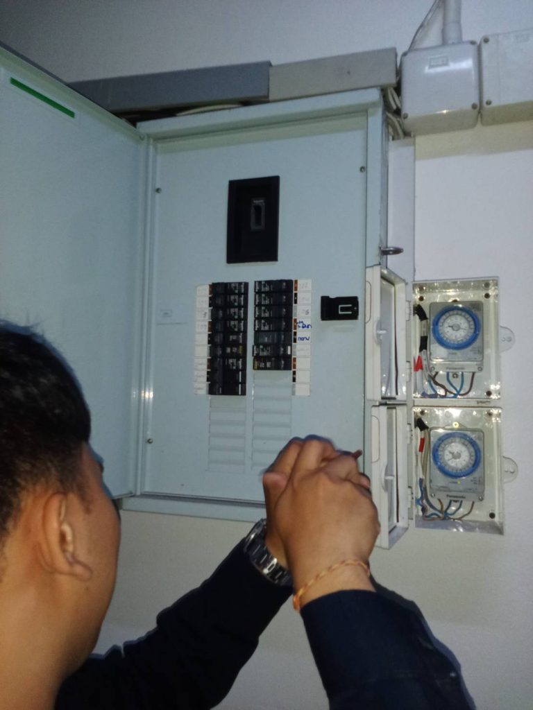 An electrician is checking an electrical panel with circuit breakers and timer switches.